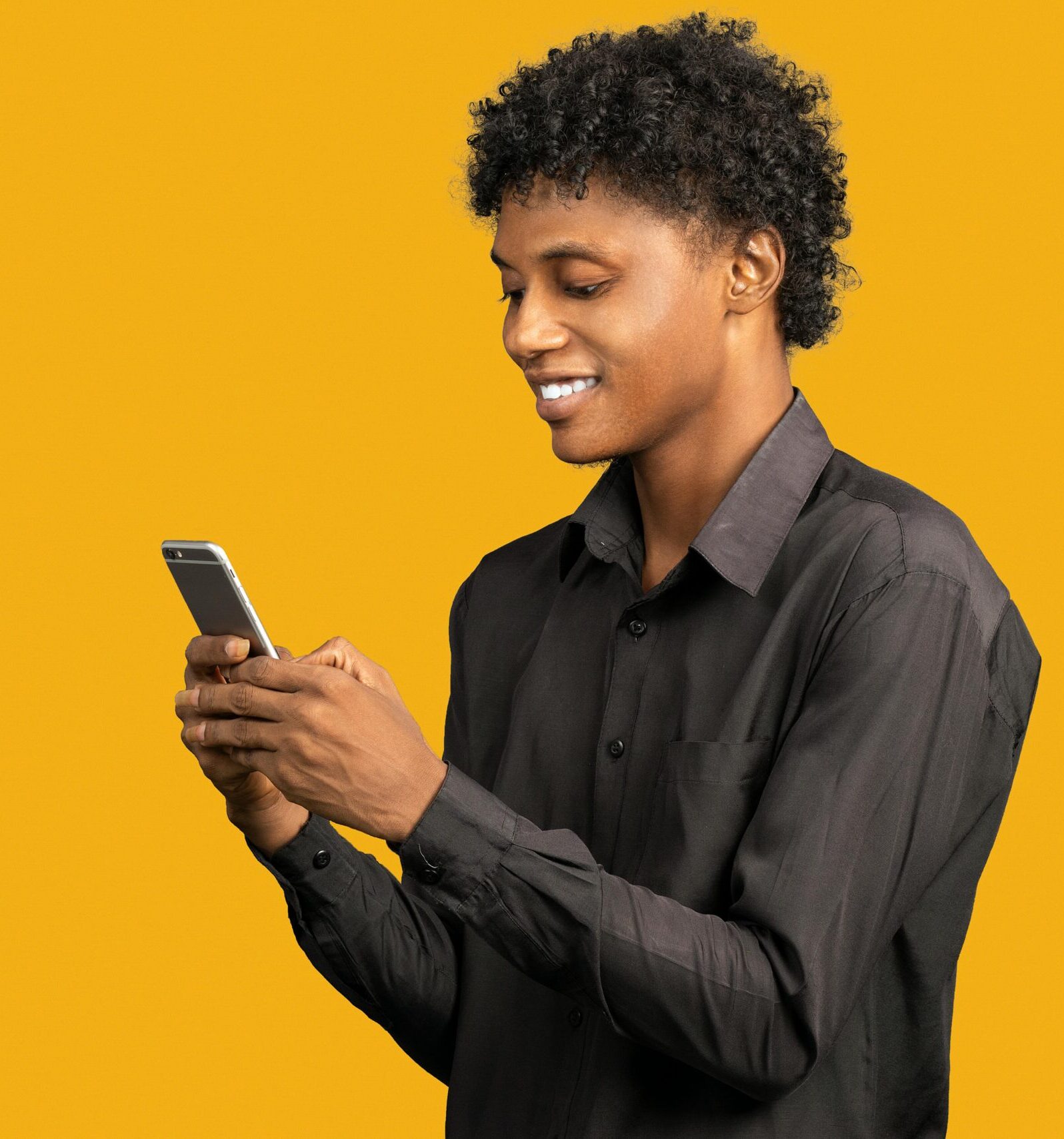 African American man in black shirt smiling while using smartphone, isolated on yellow background.