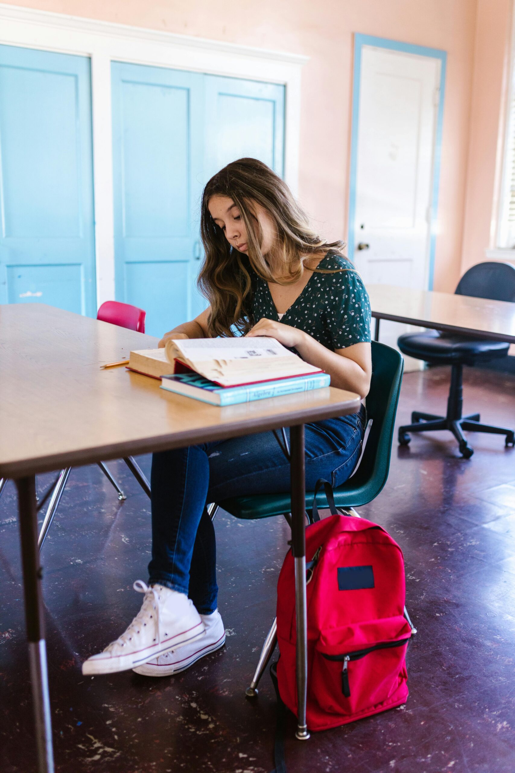 Teen girl studying in a classroom with textbooks and a vibrant red backpack.