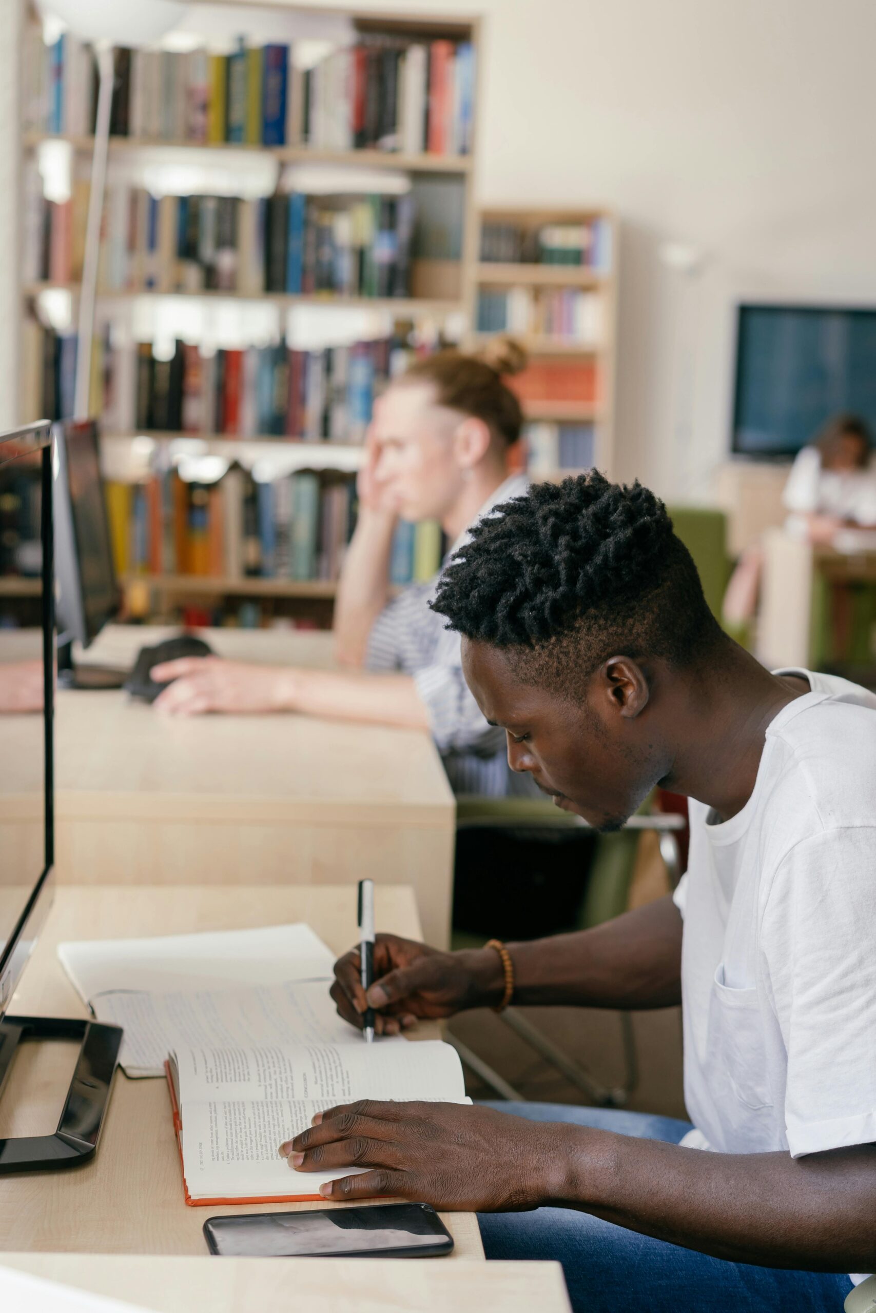 African American student intensely focused on studying with books in a bright university library.