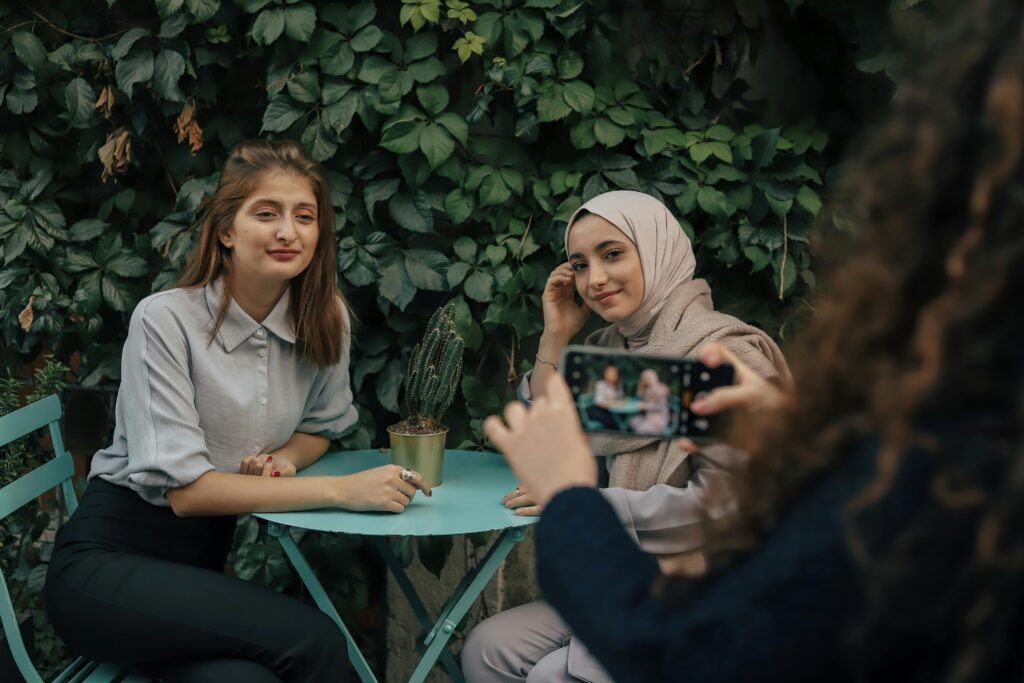 Two women sit at a cafe in Istanbul, smiling for a photo with a lush green backdrop.