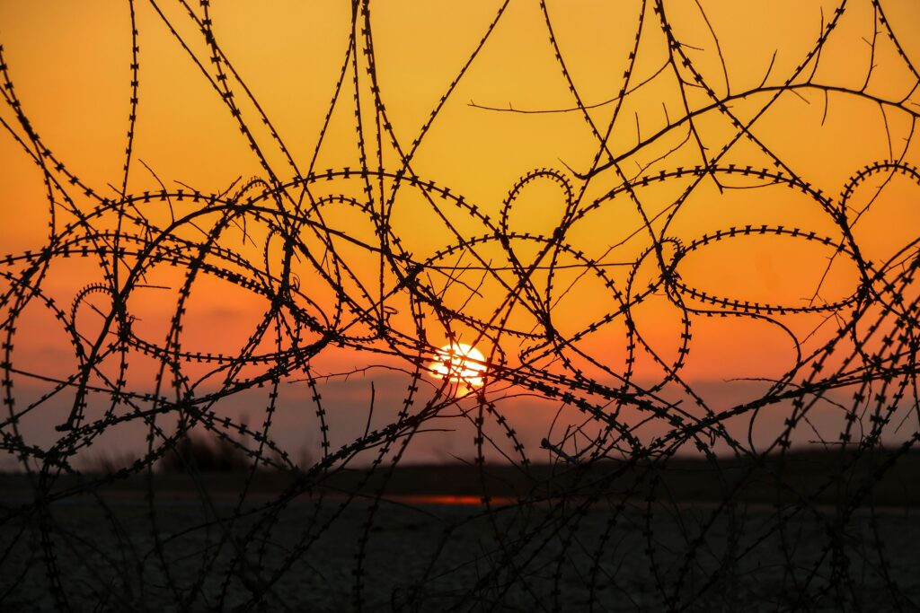 Silhouette of barbed wire against an orange sunset sky, capturing a dramatic and intense scene.