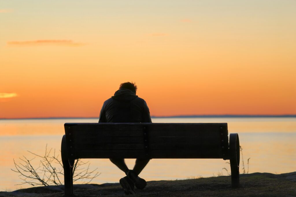 A person sits alone on a bench by the water at dawn, reflecting serenity and solitude.