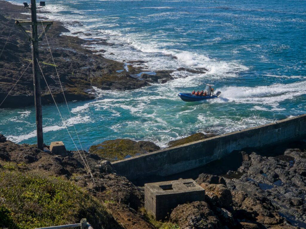 A small motorized boat navigates a rugged coastal area under the bright daytime sun.