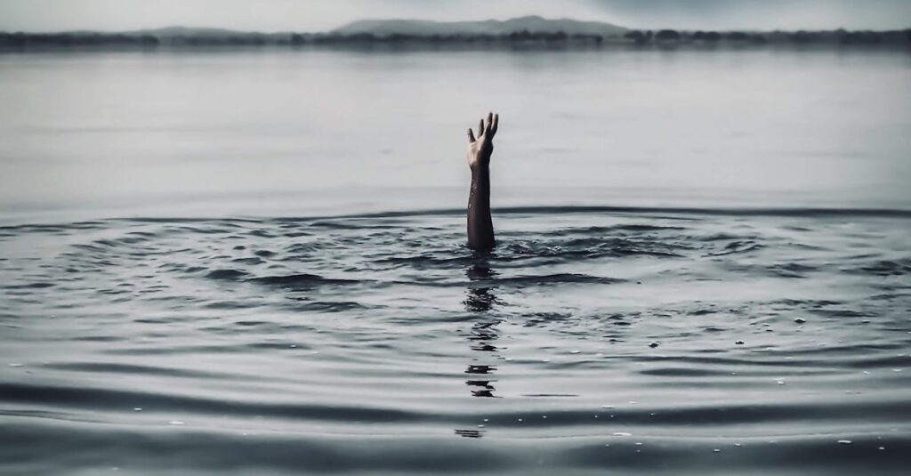 A single hand emerges from a vast body of water under a dramatic sky, symbolizing struggle and hope.