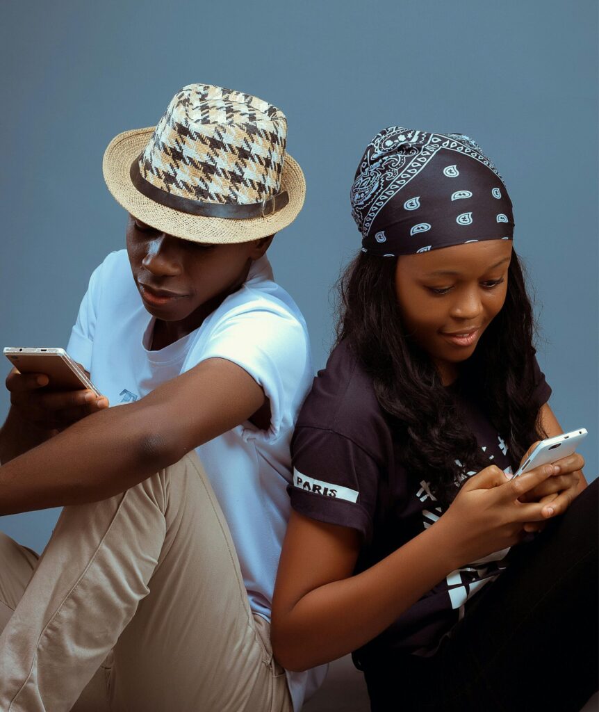 Two teenagers sitting back to back engaging with smartphones in a studio.