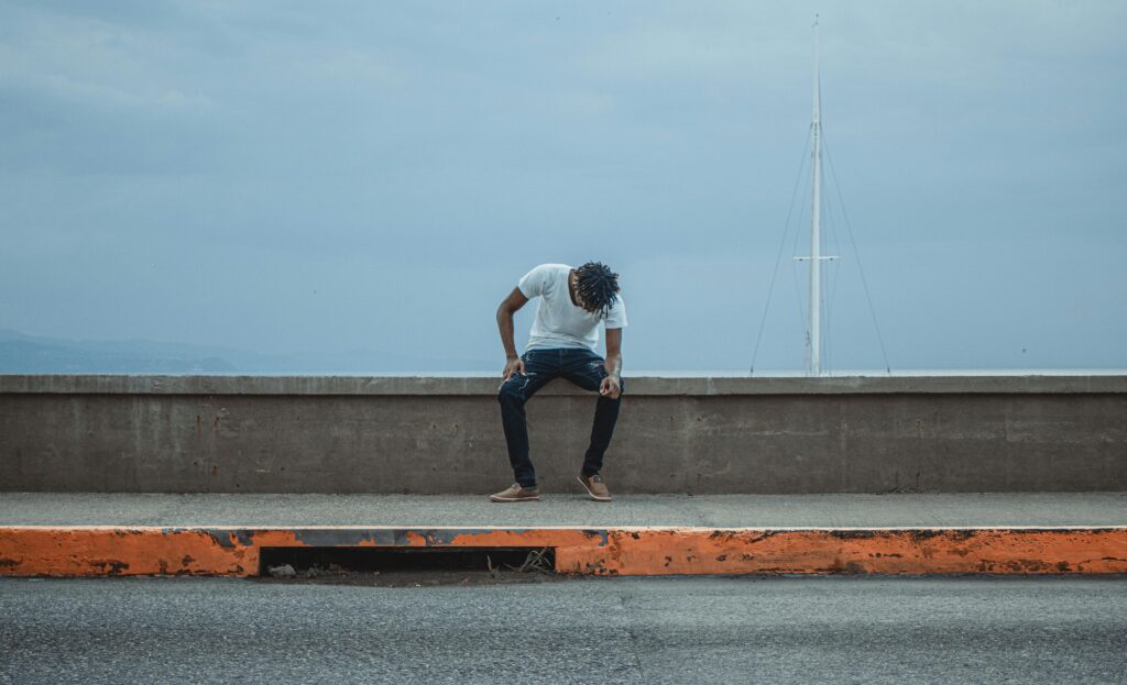 A man in a white shirt sits alone against a seawall, evoking feelings of solitude.