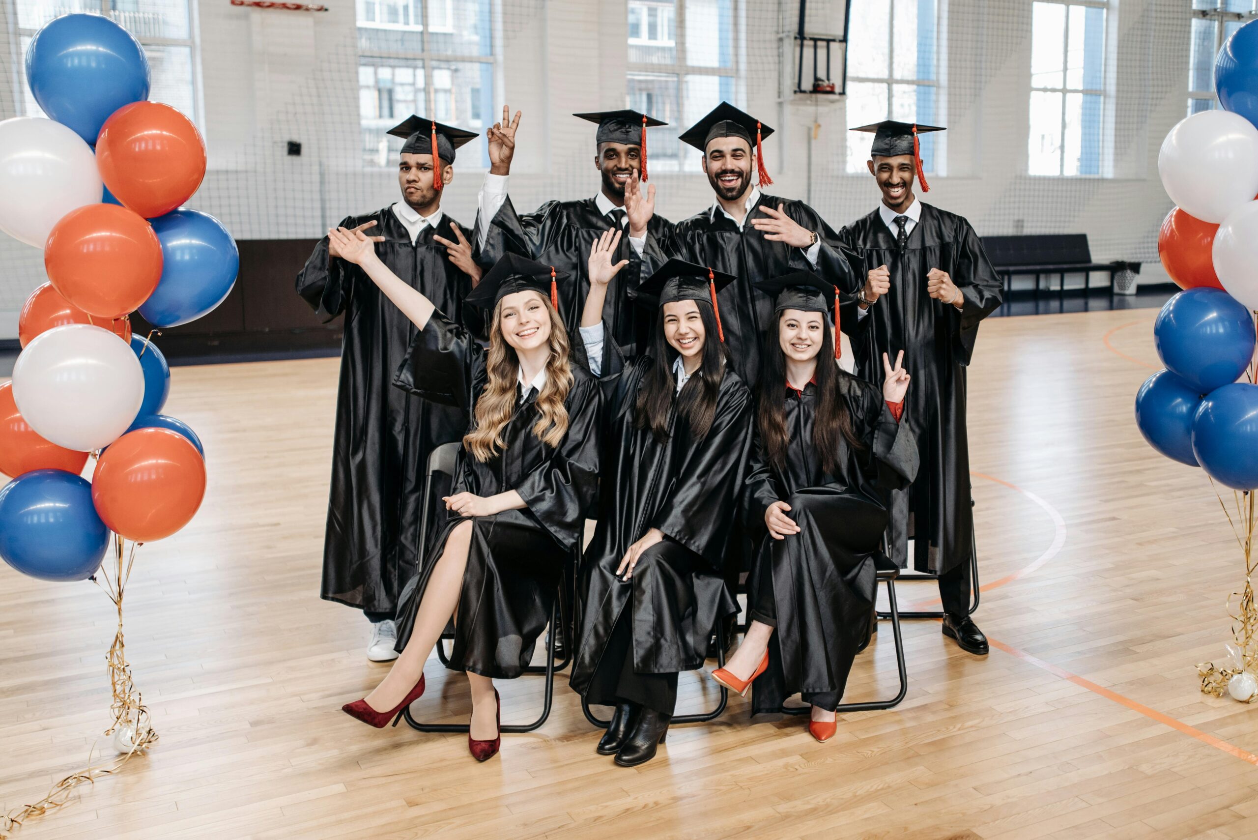 Group of diverse graduates celebrating their achievement with balloons in a gymnasium.