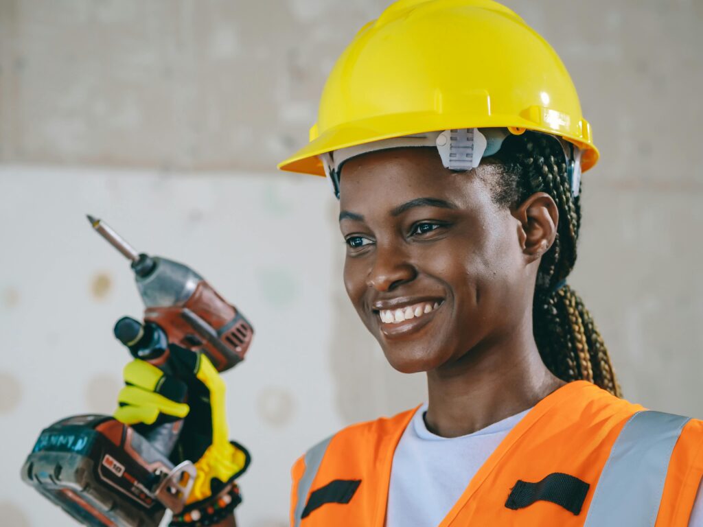 Confident female construction worker in safety gear smiling indoors.