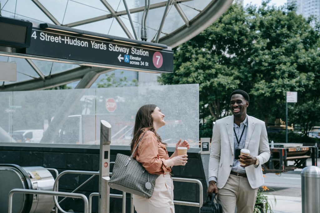 Two professionals chatting happily at Hudson Yards subway station holding coffees.