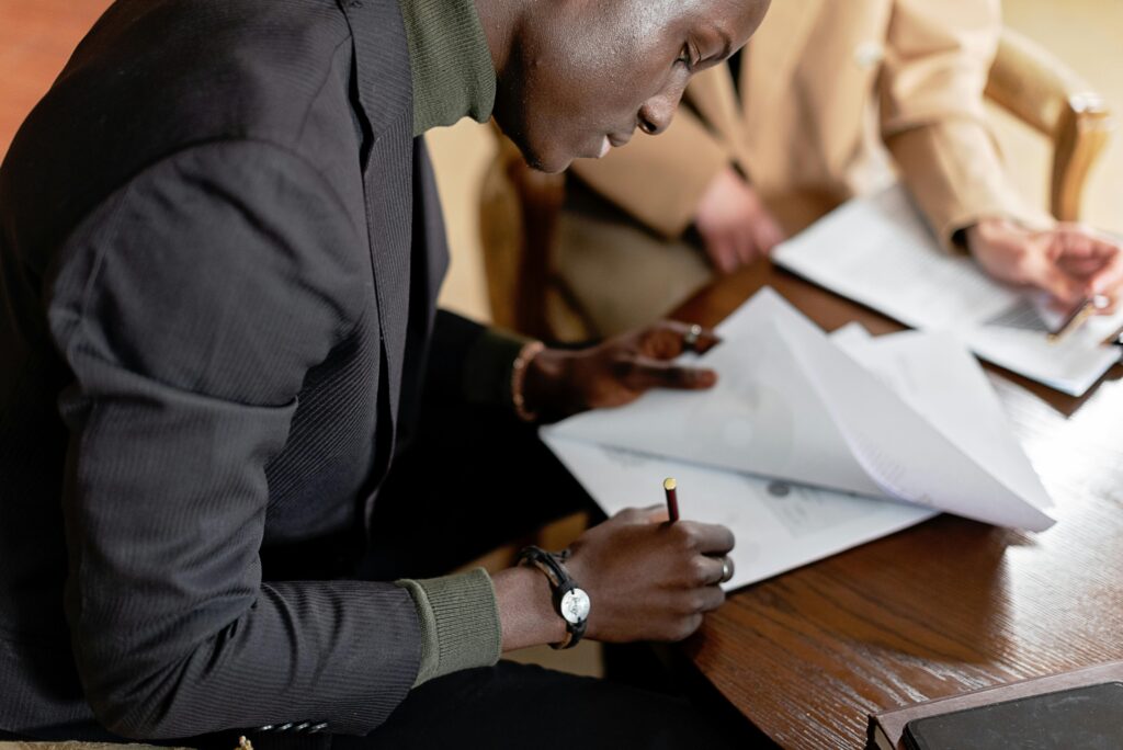 African American man focused on signing important business documents at a desk.